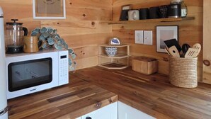 A compact kitchen with wooden walls, a coffee press, a microwave, and various kitchen utensils on shelves.