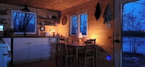 A cabin interior with a dining area, kitchen, and large windows. - Lakeview Property on Indian Lake NB Canada (Sheffield)