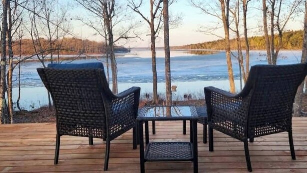 A wooden deck with two wicker chairs and a small table, overlooking a body of water and trees.