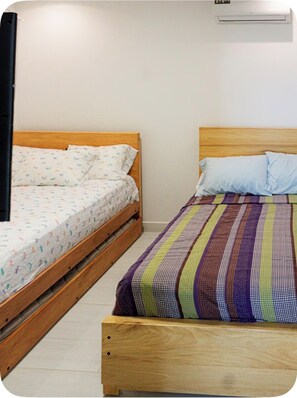Ein Zimmer mit zwei Holzbetten, eines mit einem gemusterten Überwurf und das andere mit einem Streifenmuster.