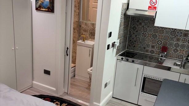Een compacte hotelkamer met een bed, een kleine kitchenette, een badkamer en een deur naar een andere kamer.
