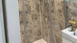 Een douche met een glazen deur, een handdouche, een douchekop aan de muur, en een handdouche op een wandbeugel.