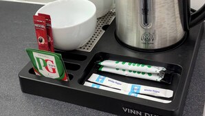 Een keukenhoek met een koffiezetapparaat van Vinn Dunn, twee witte bekers, en een dienblad met PG Tips theezakjes en Nescafe Original koffiecups.