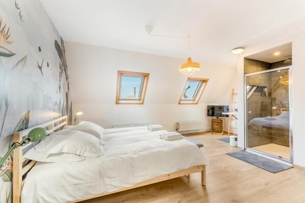 A bedroom with a bed, skylights, a green desk lamp, and a glass door leading to a bathroom. - Werf72 (Bruges)