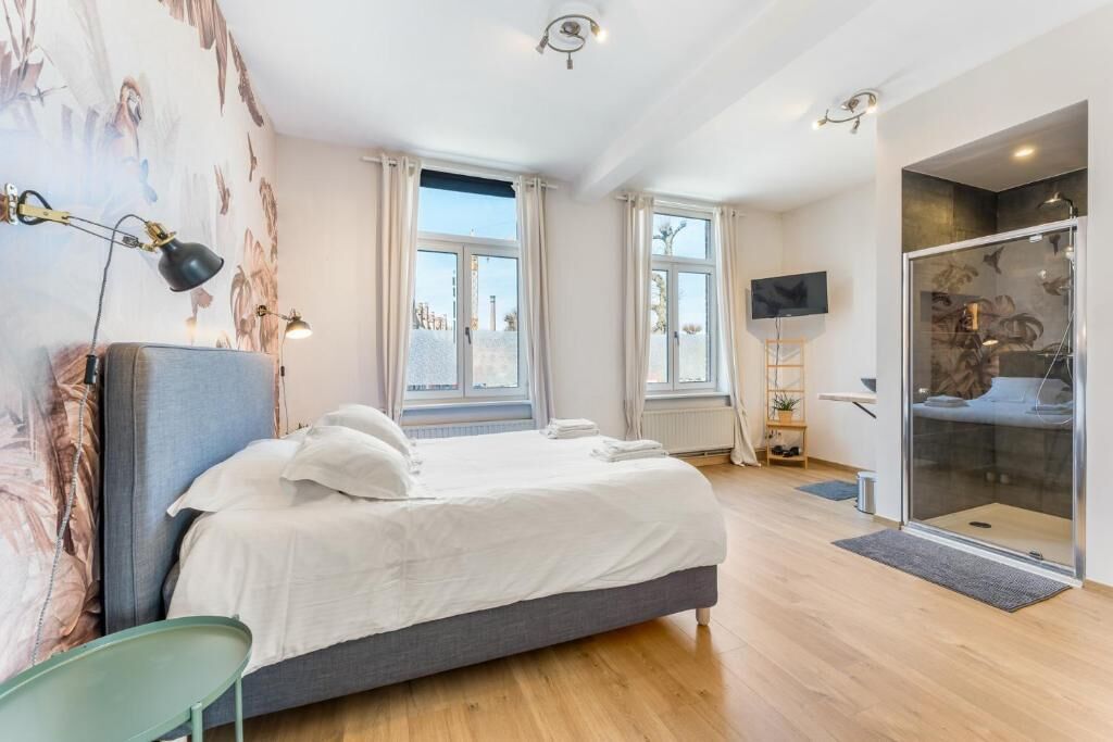 A bedroom with a bed, a TV, a shower, and a window.