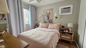 Een slaapkamer met een bed, nachtkastjes, een airconditioner aan de muur en een raam met gordijnen.