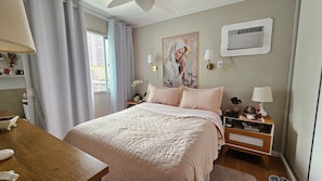 Une chambre à coucher comprenant un lit, des tables de chevet, un climatiseur fixé au mur et une fenêtre avec des rideaux.