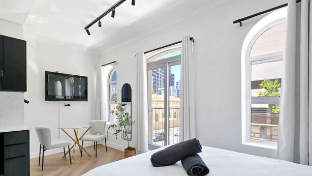 Camera d'albergo moderna con un ampio letto, una TV a schermo piatto, una scrivania con sedie e un balcone con vista sulla città.