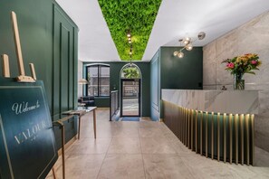 A reception area with a green wall, a reception desk, a wall-mounted light fixture, and a door leading outside. - Chic Valour studio in De Waterkant (Cape Town)