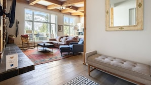 Un salon chaleureux avec une cheminée, une grande fenêtre donnant sur les arbres, un canapé, une table basse et un miroir au mur.