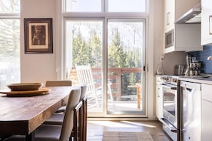 A kitchen with a large window, a dining table, chairs, and a view of trees and a deck outside. - Mountainside Top Floor Condo - Treetops Lionshead (Vail)