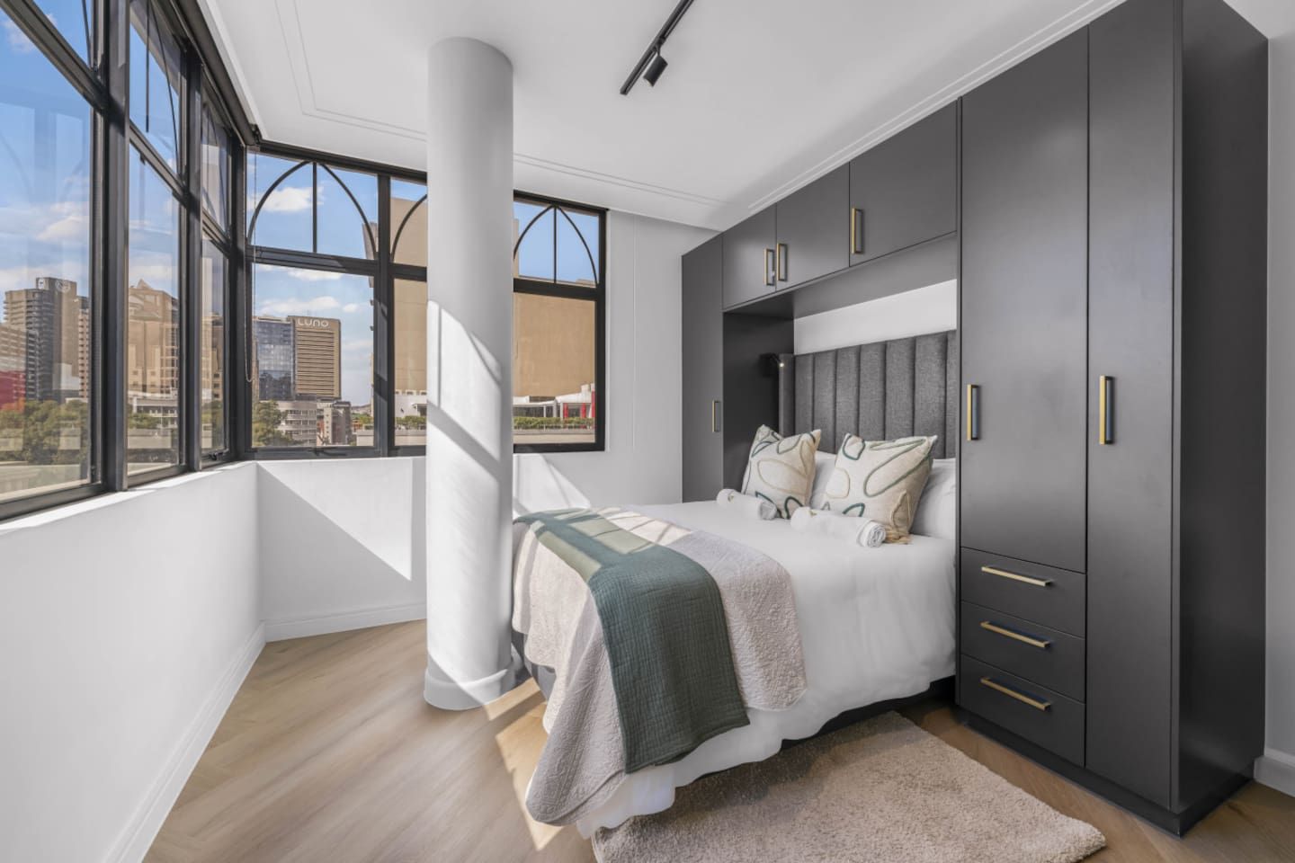 A modern bedroom with a large bed, built-in wardrobe, and a city view.