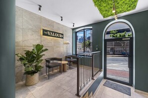 A reception area with a sign reading 'The Valour,' a potted plant, seating, and a view of the street through a glass door. - Corner Suite The Valour in De Waterkant (Cape Town)