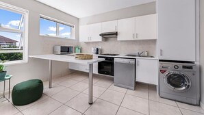 A modern kitchen with white cabinets, a dishwasher, a microwave, a stove, and a washing machine. - Little Daisy Apartment in Tamboerskloof (Cape Town)