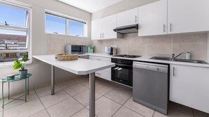 A modern kitchen with white cabinets, a microwave, a stove, and a dishwasher. - Little Daisy Apartment in Tamboerskloof (Cape Town)