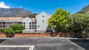 A multi-story building with a flat roof, a parking lot in front, and a mountainous backdrop. - Little Daisy Apartment in Tamboerskloof (Cape Town)