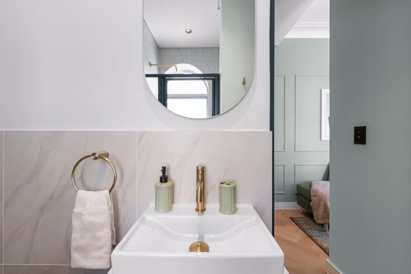 A modern bathroom with a white sink, gold fixtures, a towel ring, and a mirror.
