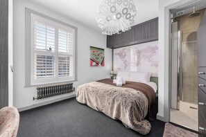 A bedroom with a bed, a radiator, a window with blinds, a world map on the wall, and a shower. - Stylish Hale home 2 bedroom (Hale)
