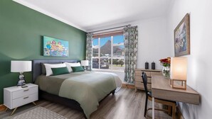 Ein Schlafzimmer mit Bett, Nachttischen, einem Schreibtisch, einem Stuhl, einem Fenster mit Blick und einem Bild an der Wand.