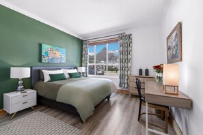 Een slaapkamer met een bed, nachtkastjes, een bureau, een stoel, een raam met uitzicht en een schilderij aan de muur.