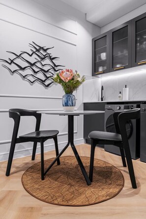A modern kitchen with a round table, two chairs, a vase with flowers, and a decorative wall piece. - Valour Suite in De Waterkant (Cape Town)