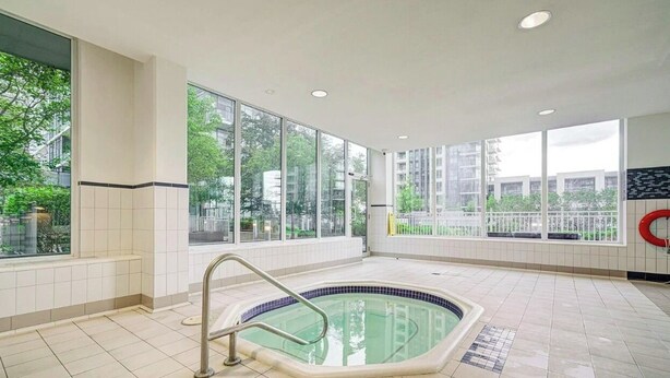 Ein Schwimmbecken mit Metallleiter, großen Fenstern und Blick auf Gebäude und Bäume.