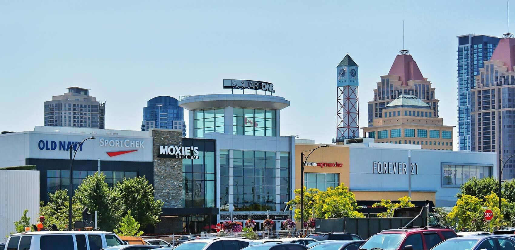 Vista urbana com edifícios, incluindo um restaurante chamado 'Moxie's Grill Bar' e um hotel chamado 'Forever 21'.