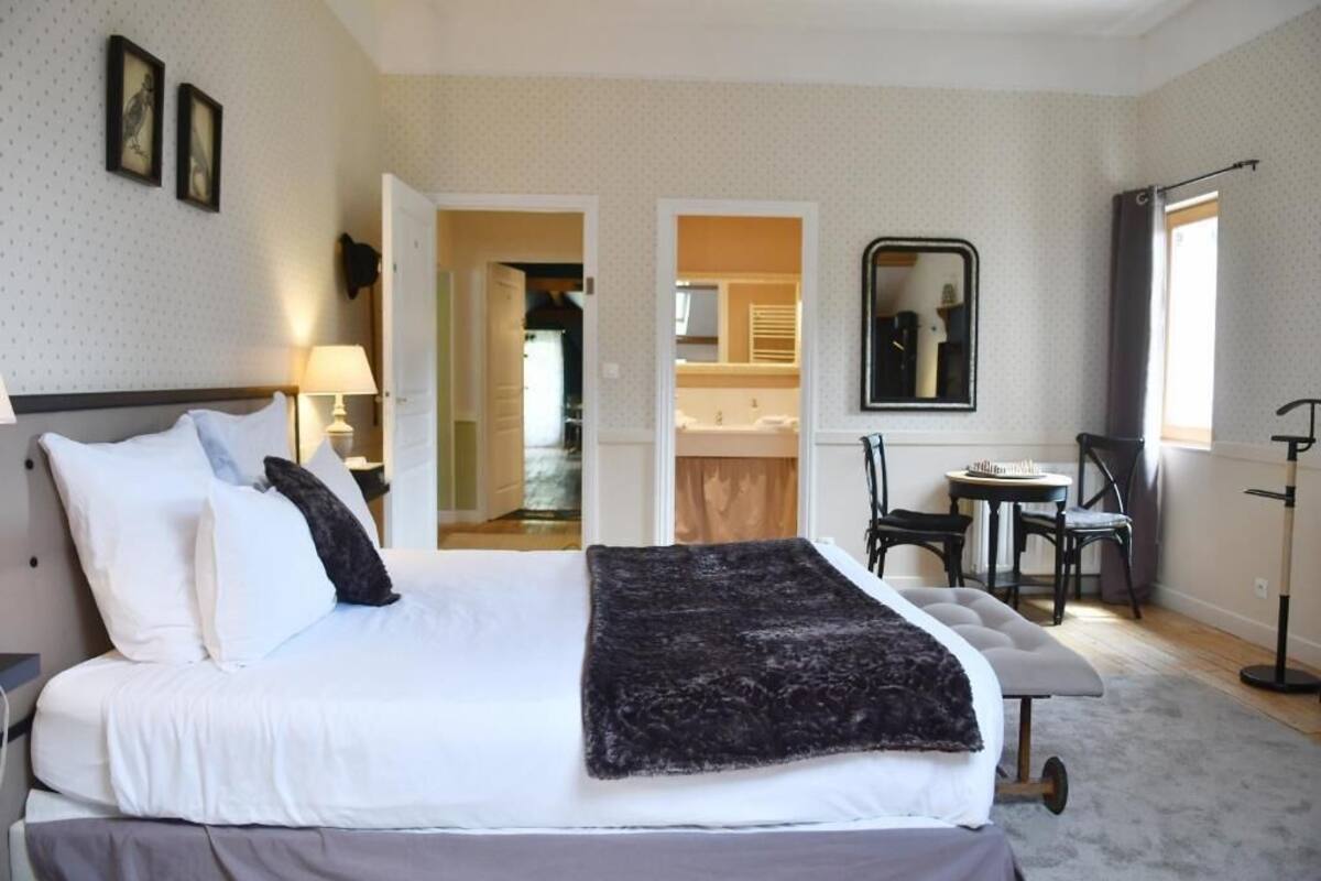 Une chambre à coucher avec un lit, une table de chevet, une lampe, et une vue sur la salle de bain et la cuisine, grâce à une porte ouverte.