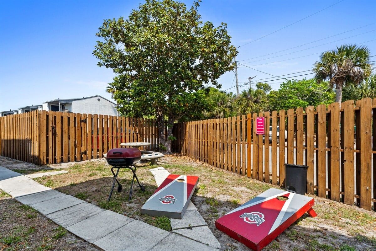 A backyard with a wooden fence, a barbecue grill, and two corn hole boards.