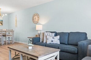 Ein Wohnzimmer mit grauem Sofa, Holztisch und Wanduhr.