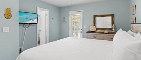 A bedroom with a bed, a ceiling fan, a television, and a door leading to another room.