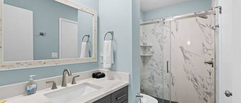 A bathroom with a white sink, a mirror, a shower with marble walls, and a toilet.