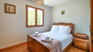 A bedroom with a wooden bed, a window, a chandelier, and a small wooden nightstand. - Cozy Detached House with Mountain View, WiFi & Parking (Saint-Pierre-d'Albigny)