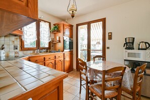 Una cocina con armarios de madera, salpicadero de azulejos, una mesa de comedor con sillas y una cafetera.