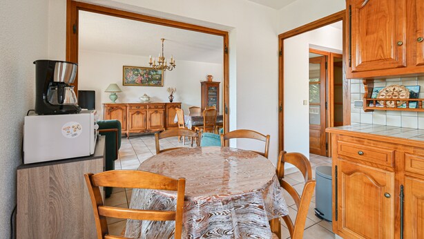 A dining area with a round table, chairs, a coffee machine, and wooden cabinets. - Cozy Detached House with Mountain View, WiFi & Parking (Saint-Pierre-d'Albigny)