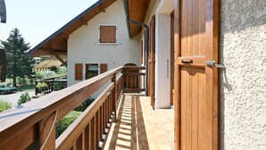 A wooden balcony with a view of a building with a sloped roof and a door. - Cozy Detached House with Mountain View, WiFi & Parking (Saint-Pierre-d'Albigny)