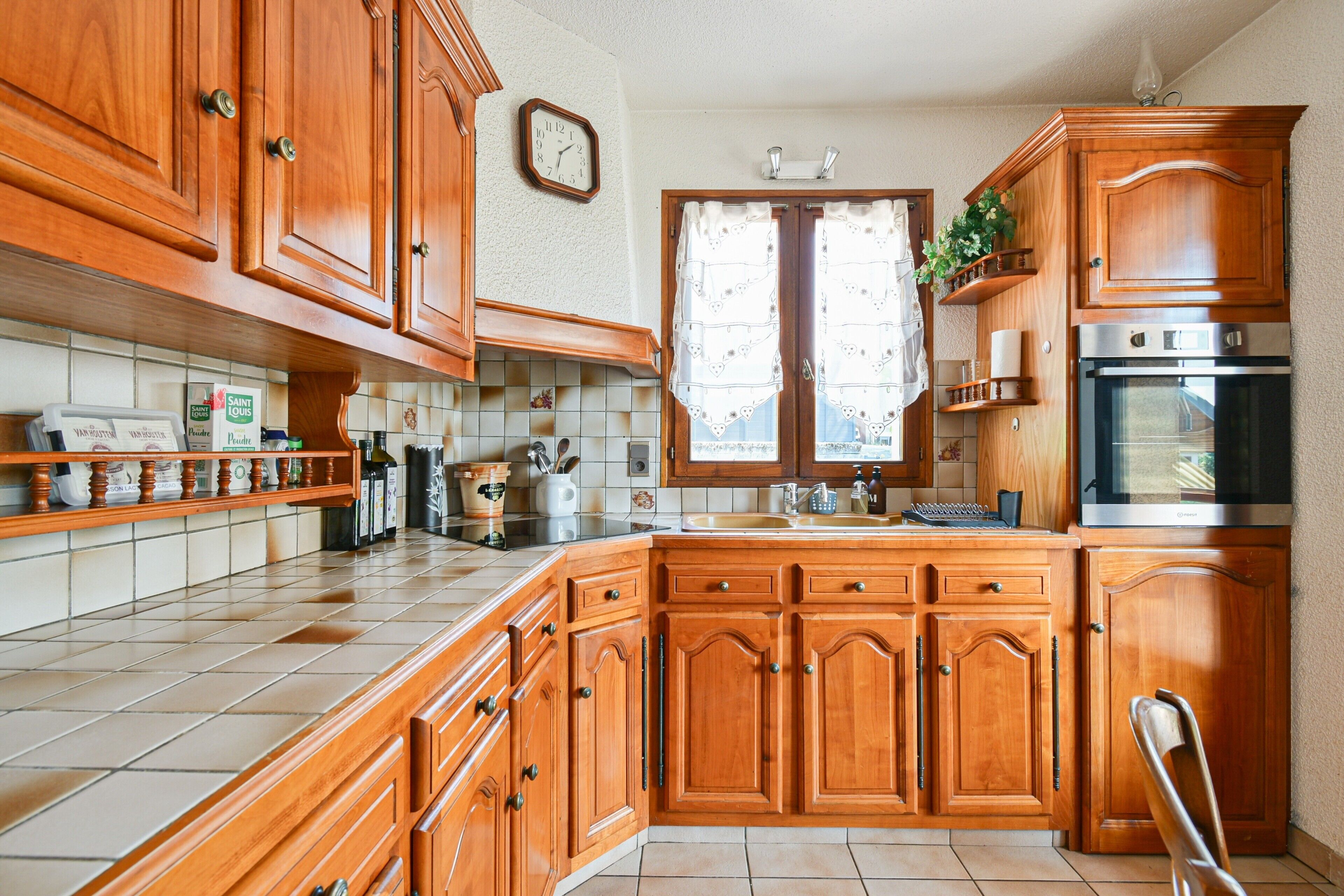Une cuisine avec des meubles en bois, un four en acier inoxydable et une fenêtre avec un rideau.