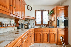 A kitchen with wooden cabinets, a stainless steel oven, and a window with a curtain. - Cozy Detached House with Mountain View, WiFi & Parking (Saint-Pierre-d'Albigny)
