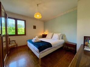 A bedroom with a bed, a window, a wooden floor, a hanging light fixture, and a wooden chair. - Cozy Detached House with Mountain View, WiFi & Parking (Saint-Pierre-d'Albigny)