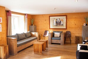 Een kamer met houten lambrisering, een bank, twee stoelen, een kleine tafel en een lijst met een afbeelding aan de muur.
