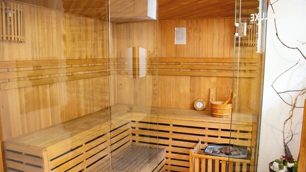 A sauna with wooden walls and benches, a clock, and a small wooden table with a bowl.