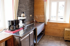 A kitchen with stainless steel appliances, a wooden wall, and a window with curtains.