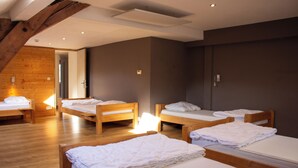 A room with four wooden beds, each with white linens, and a wooden ceiling structure.