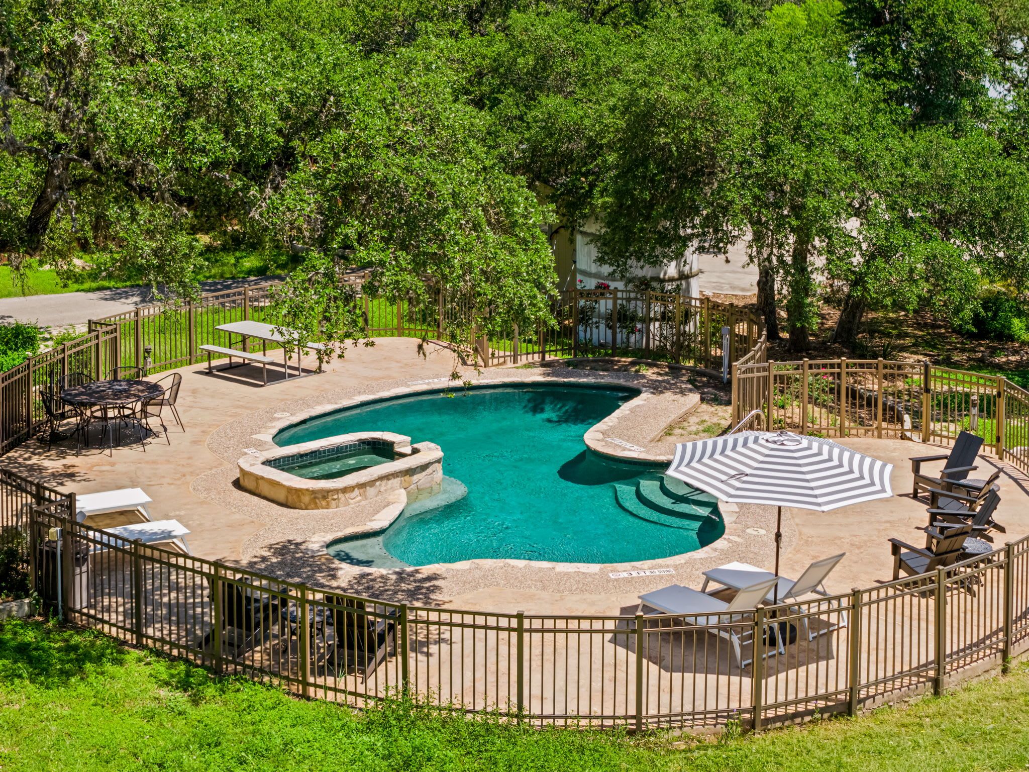 A circular pool with a hot tub, surrounded by a fence, and equipped with outdoor furniture.