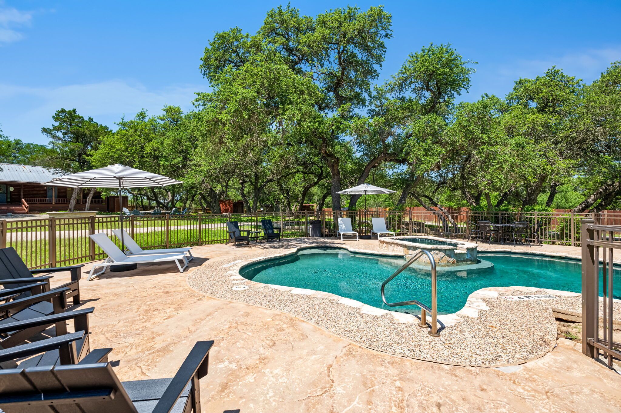 Ein Pool mit Liegestühlen und Sonnenschirmen, umgeben von Bäumen und einem eingezäunten Bereich.