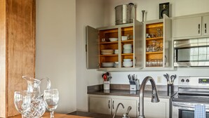 Una cucina con piano di lavoro in legno, elettrodomestici in acciaio inossidabile e pensili aperti con stoviglie e bicchieri.