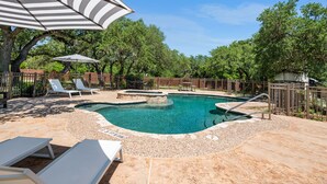 Una piscina con lettini e un ombrellone, circondata da una recinzione in legno e alberi.