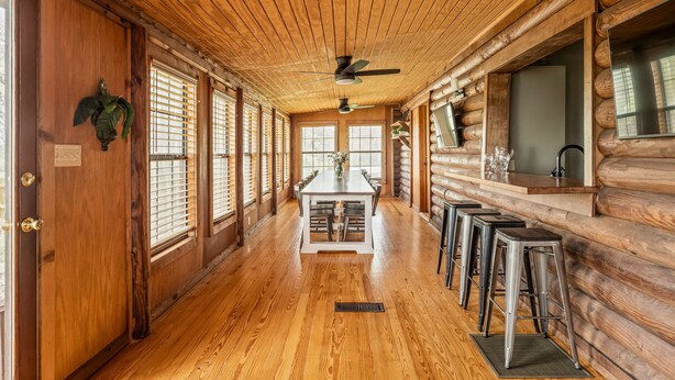 Interno di una baita di legno con un tavolo da pranzo, sgabelli da bar, pavimento in legno e una ventola a soffitto.