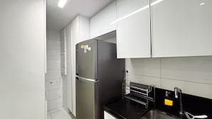 Una cocina moderna con armarios blancos, un refrigerador de acero inoxidable y una encimera negra.