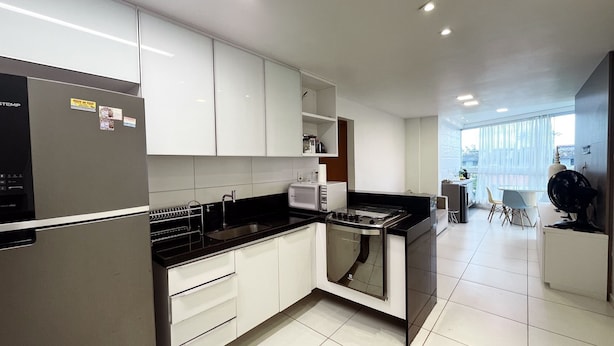 Una cocina moderna con armarios blancos, encimera negra y horno integrado.